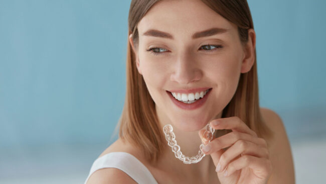 Junge, braunhaarige Frau mit Zahnschiene in der Hand, blauer Hintergrund