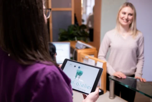 Close up ZFA von hinten mit Tablet in der Hand. Vor ihr steht eine lächelnde Patientin