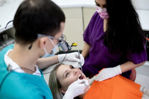 Close up Patientin mit offenem Mund wird mit Zahnarztbesteck von Dimitri Tanurcov und einer ZFA behandelt