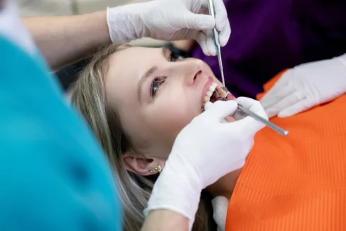 Close up Patientin mit offenem Mund wird mit Zahnarztbesteck behandelt